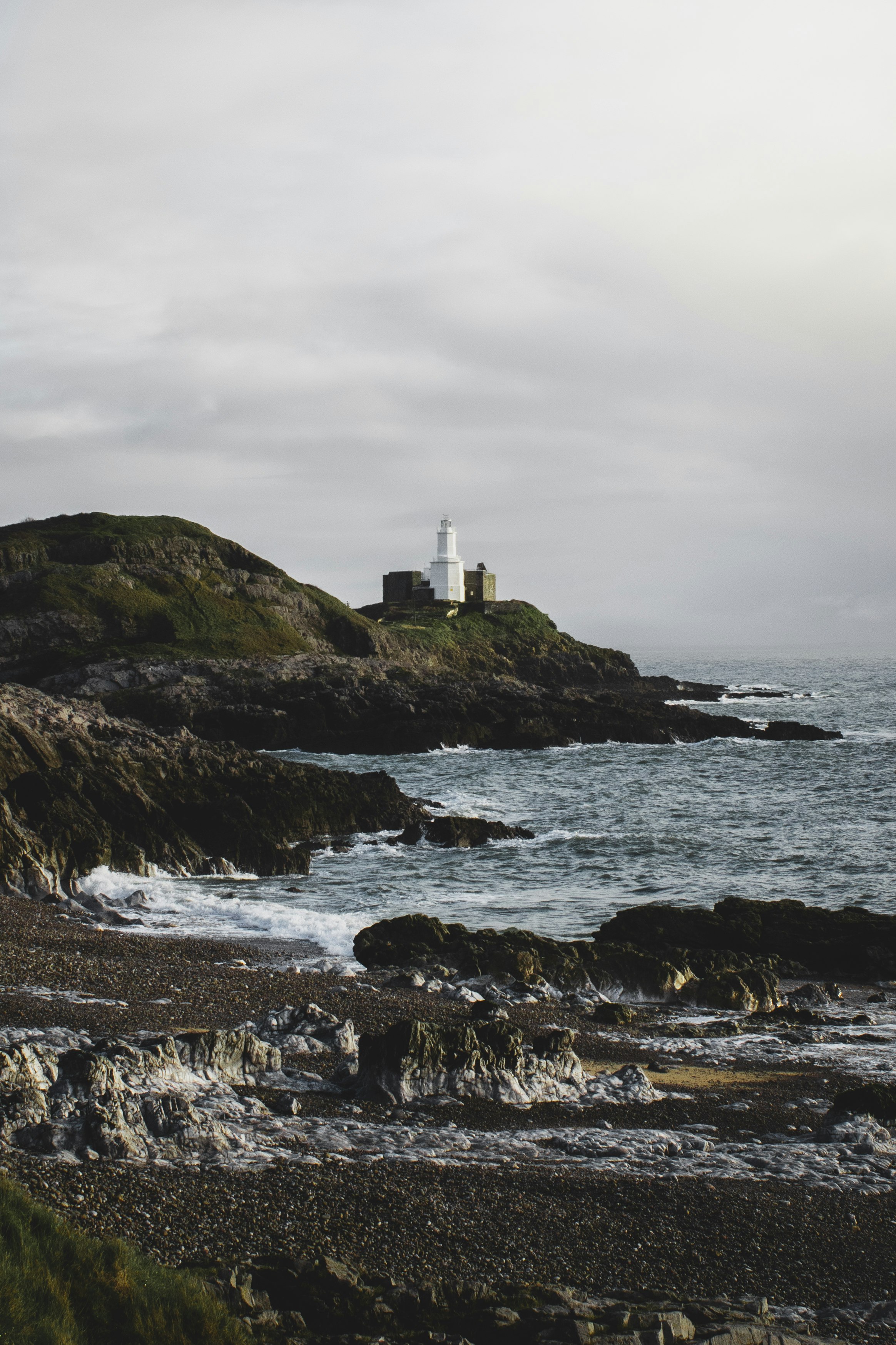 white lighthouse on top of the hill by the sea under white clouds during daytime